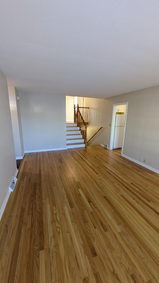 unfurnished living room with light wood-type flooring, visible vents, and baseboards