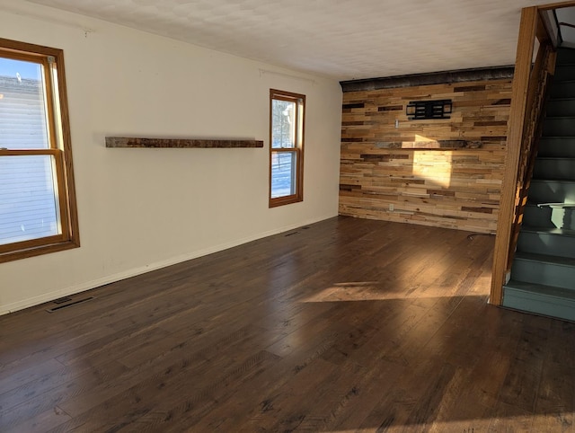 spare room with wooden walls, visible vents, baseboards, wood-type flooring, and stairway