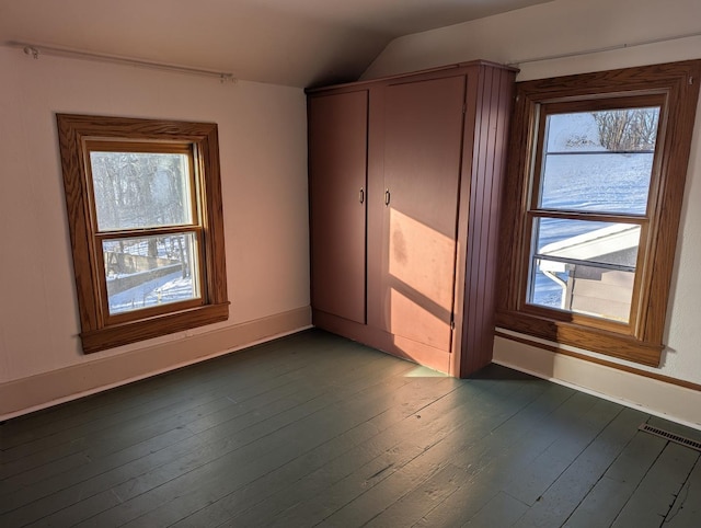 unfurnished bedroom with dark wood-type flooring, a closet, vaulted ceiling, and baseboards