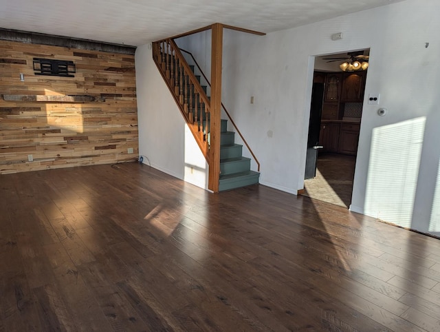 unfurnished room with hardwood / wood-style flooring, stairs, wooden walls, and a ceiling fan