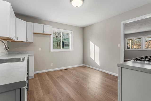 kitchen featuring baseboards, light wood finished floors, a sink, and white cabinets