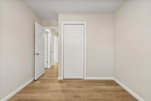 unfurnished bedroom featuring a closet, light wood-style flooring, and baseboards