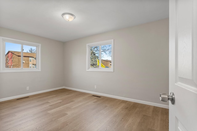 unfurnished room featuring a wealth of natural light, visible vents, light wood finished floors, and baseboards