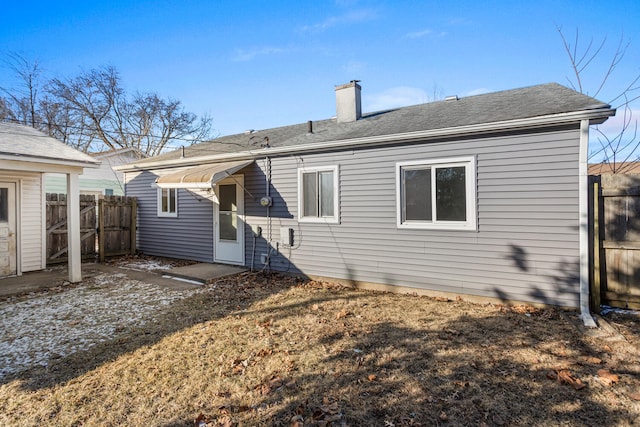 rear view of house with roof with shingles, fence, and a chimney