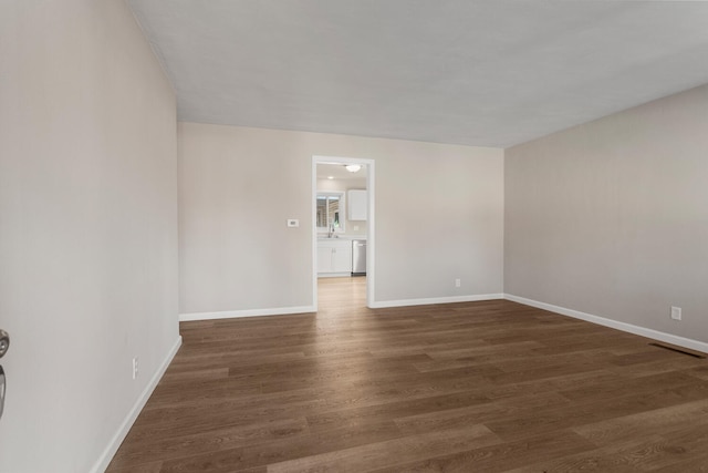 spare room with dark wood-style flooring, a sink, and baseboards