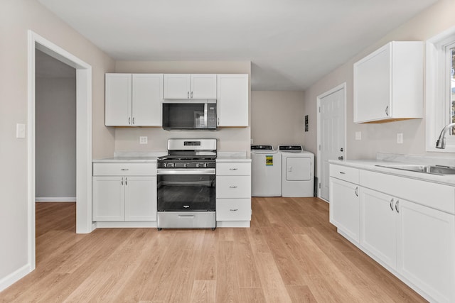 kitchen with stainless steel appliances, separate washer and dryer, a sink, white cabinetry, and light countertops