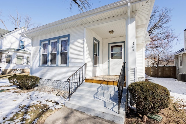 snow covered property entrance with covered porch, central AC, and fence