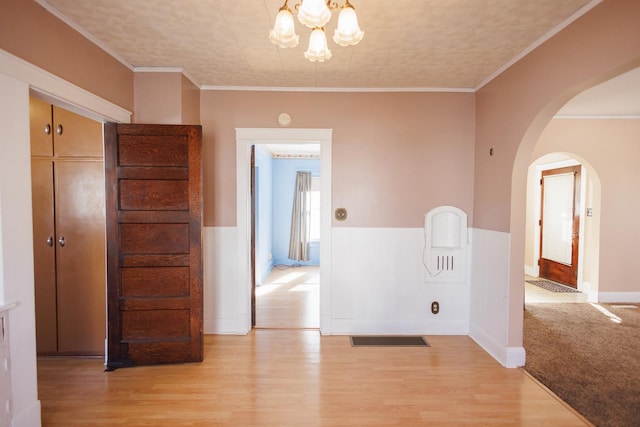 unfurnished room featuring arched walkways, crown molding, light wood-style flooring, wainscoting, and a chandelier