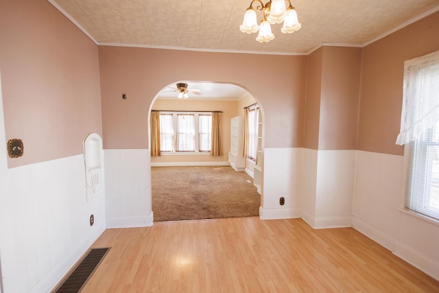 empty room with light wood-style flooring, visible vents, arched walkways, and ornamental molding