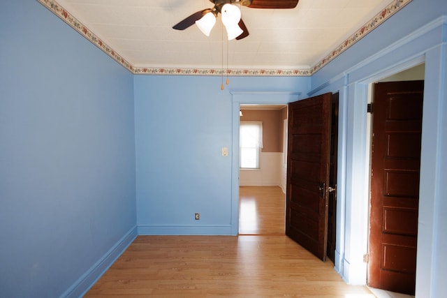 spare room featuring light wood-type flooring, ceiling fan, and baseboards