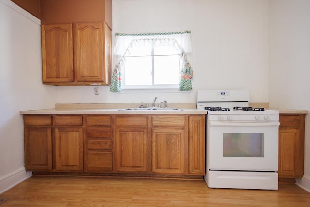 kitchen with light wood-type flooring, light countertops, white range with gas cooktop, and a sink