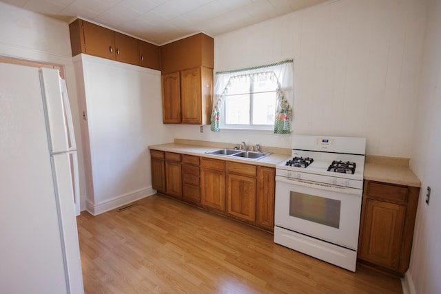 kitchen featuring light countertops, white appliances, brown cabinetry, and a sink