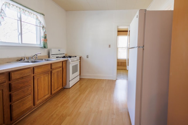 kitchen featuring light countertops, brown cabinetry, a healthy amount of sunlight, a sink, and white appliances