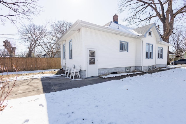 snow covered back of property featuring a chimney and fence