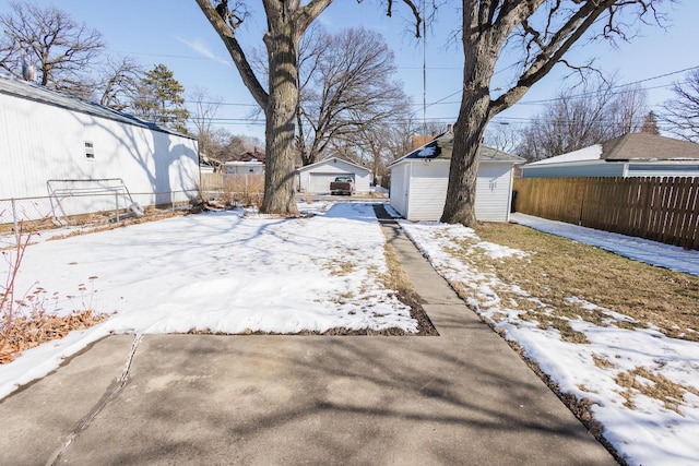 yard layered in snow with a detached garage, fence, and an outbuilding