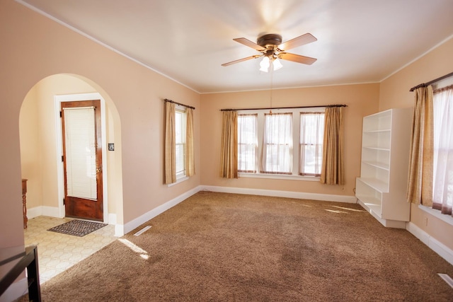 empty room with ornamental molding, arched walkways, light colored carpet, and baseboards