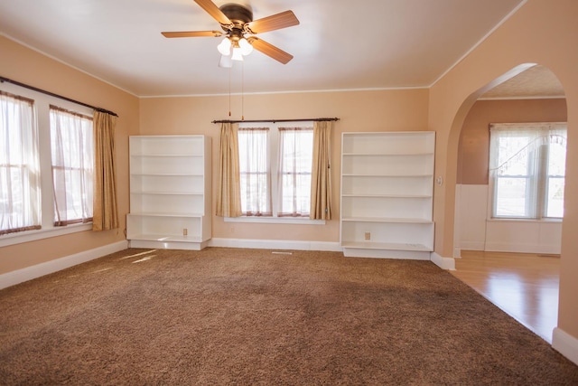 unfurnished room featuring arched walkways, ceiling fan, ornamental molding, and a wealth of natural light