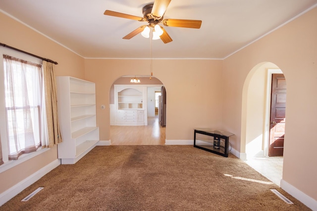 spare room featuring ornamental molding, arched walkways, light colored carpet, and baseboards