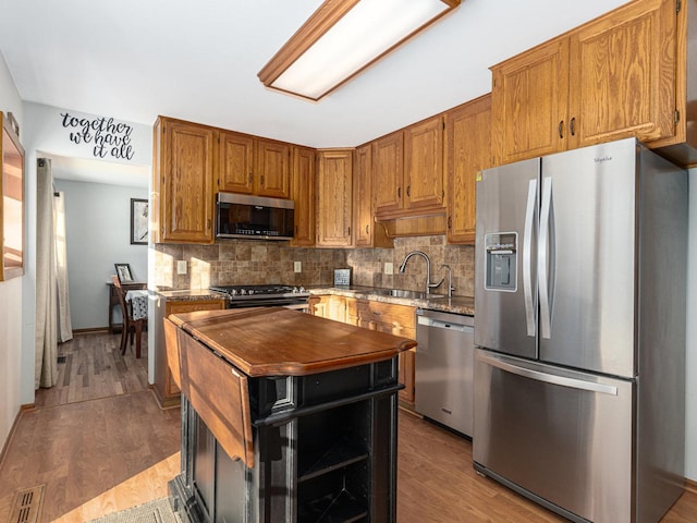 kitchen with light wood finished floors, appliances with stainless steel finishes, backsplash, and brown cabinets