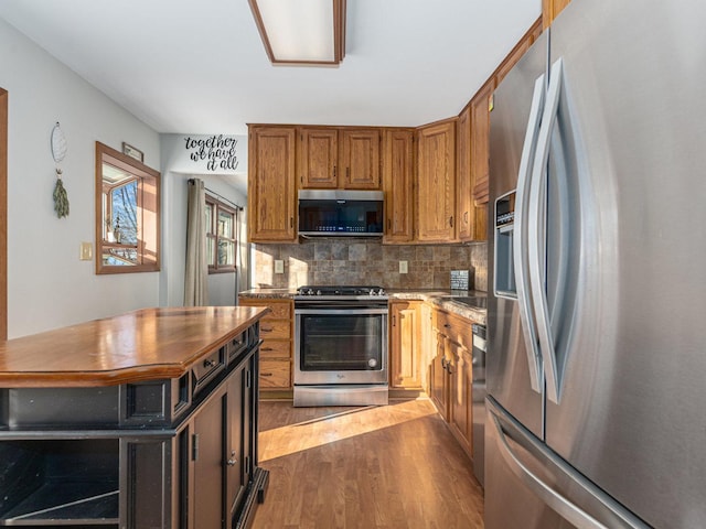 kitchen with appliances with stainless steel finishes, dark wood-style flooring, brown cabinets, and tasteful backsplash