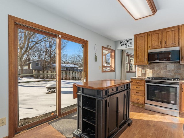 kitchen with light wood-style floors, stainless steel appliances, backsplash, and brown cabinetry