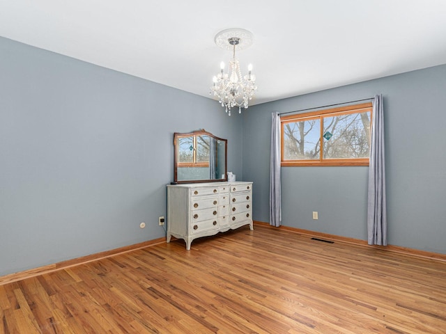 unfurnished room with a chandelier, light wood-type flooring, visible vents, and baseboards