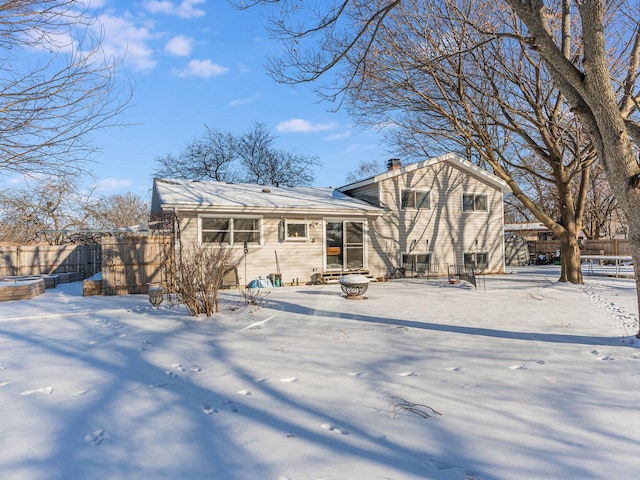 snow covered rear of property featuring an outdoor fire pit, a chimney, and fence