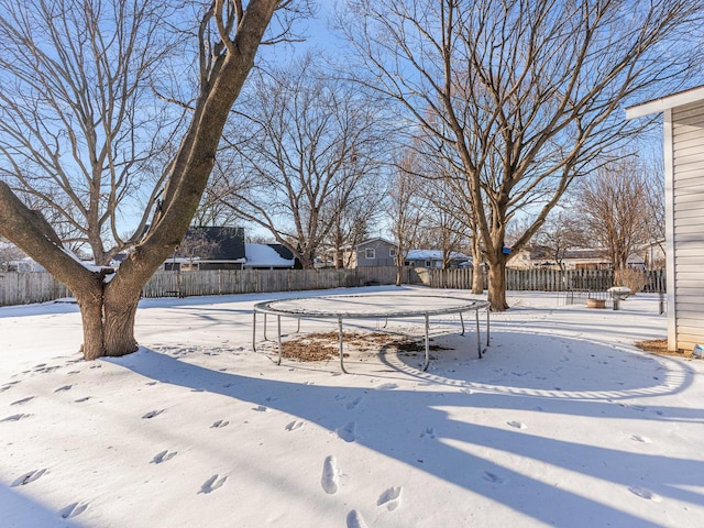 yard layered in snow featuring a trampoline and fence