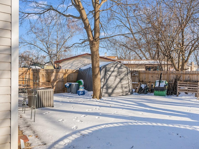 yard layered in snow with a fenced backyard, central AC, and an outbuilding