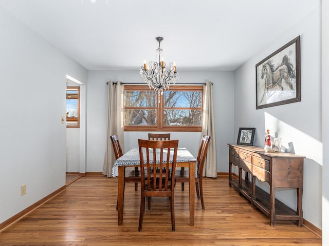 dining room with baseboards, light wood finished floors, plenty of natural light, and a notable chandelier