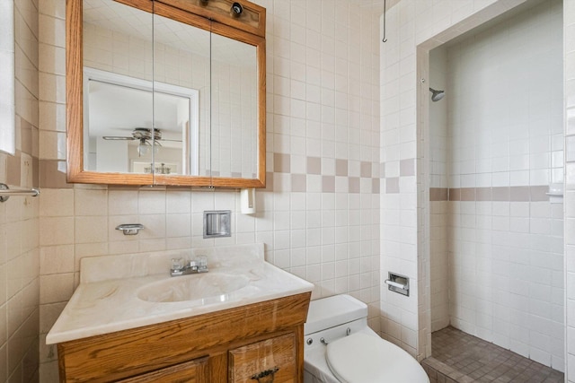 full bathroom featuring tiled shower, toilet, ceiling fan, vanity, and tile walls