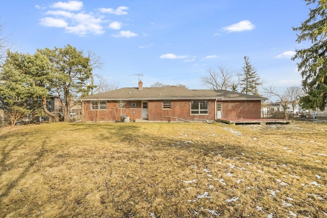 back of house with brick siding, a lawn, a chimney, and a wooden deck