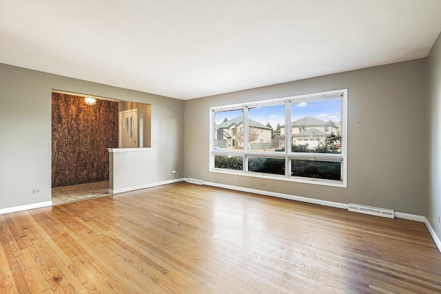 empty room with wood-type flooring, visible vents, and baseboards