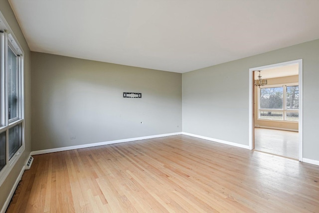 spare room with light wood-type flooring, visible vents, baseboards, and a chandelier