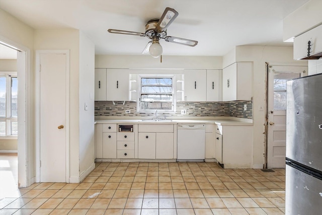 kitchen featuring decorative backsplash, dishwasher, freestanding refrigerator, light countertops, and a sink