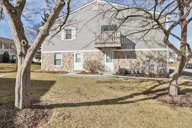 view of front facade featuring a balcony, stone siding, and a front yard