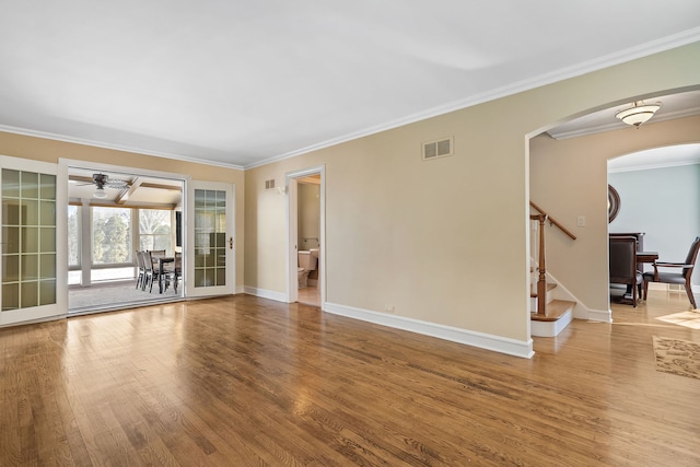 unfurnished living room with arched walkways, wood finished floors, visible vents, baseboards, and stairway