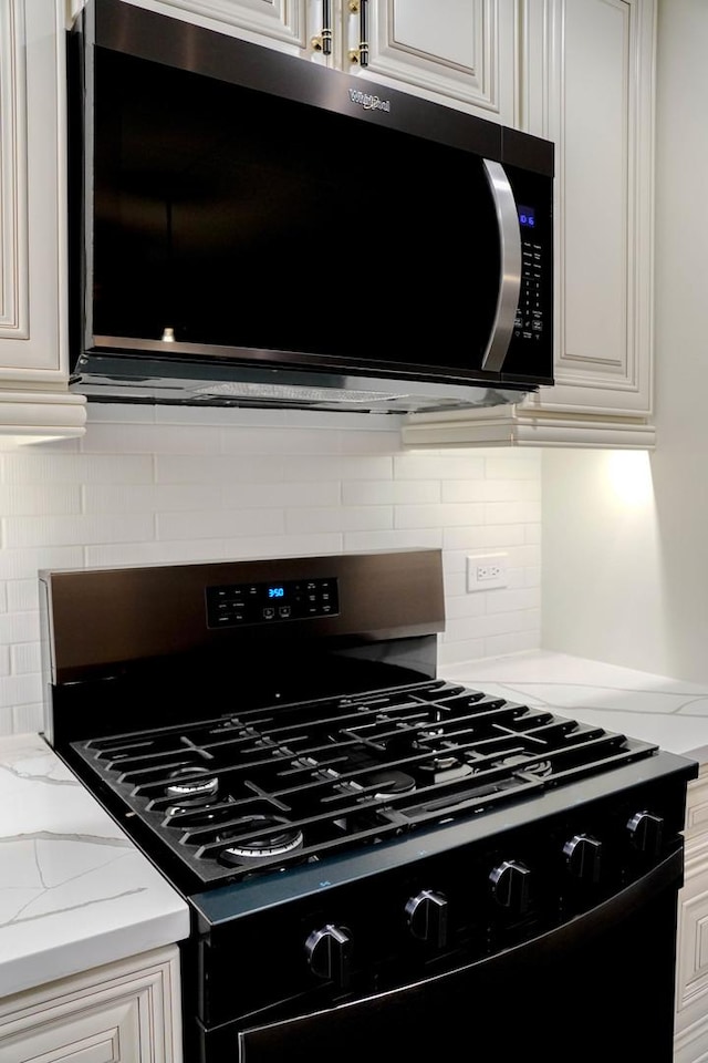 kitchen featuring light stone counters, white cabinetry, black gas range, and tasteful backsplash