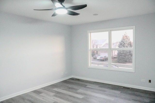 empty room featuring a ceiling fan, wood finished floors, visible vents, and baseboards