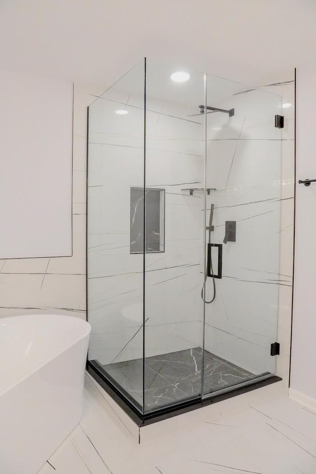 full bathroom with marble finish floor, a freestanding tub, and a shower stall