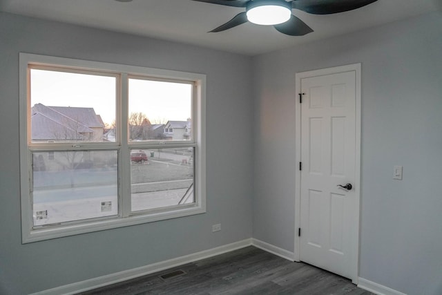 empty room with a ceiling fan, dark wood-style flooring, visible vents, and baseboards