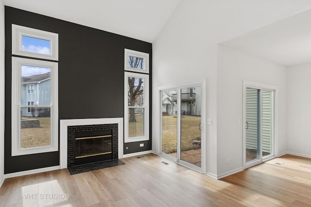 entryway featuring baseboards, visible vents, wood finished floors, a fireplace, and high vaulted ceiling