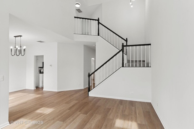 interior space featuring visible vents, a high ceiling, wood finished floors, a chandelier, and baseboards