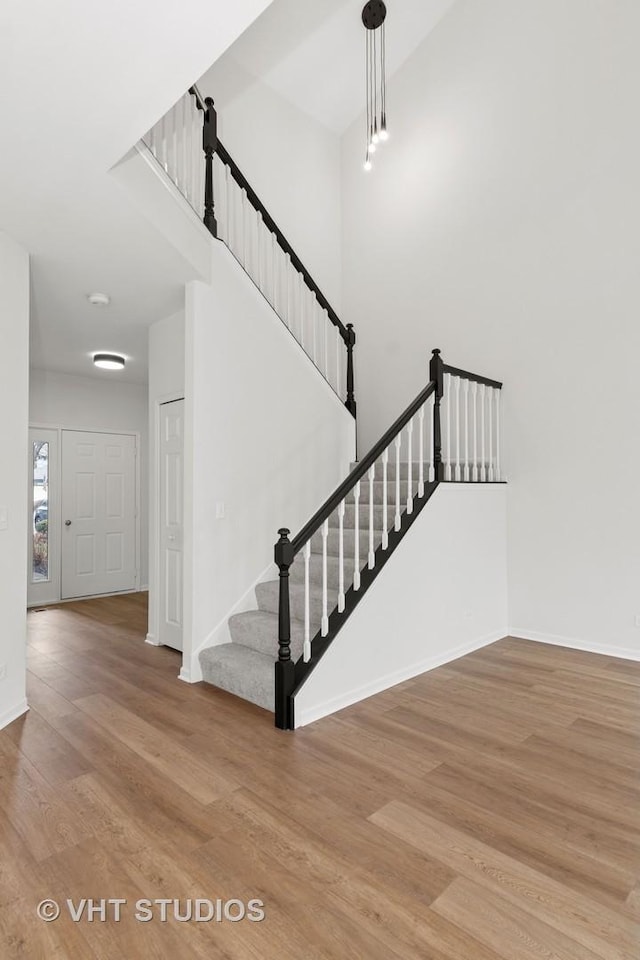 stairway featuring a high ceiling, wood finished floors, and baseboards