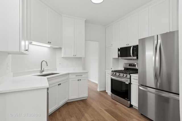 kitchen with light countertops, light wood-style flooring, appliances with stainless steel finishes, white cabinetry, and a sink