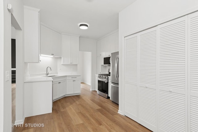 kitchen featuring light wood finished floors, light countertops, appliances with stainless steel finishes, white cabinetry, and a sink