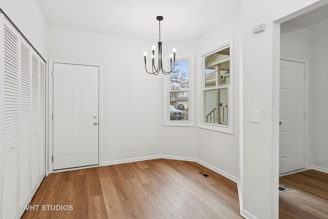 unfurnished dining area featuring visible vents, light wood-style flooring, baseboards, and an inviting chandelier