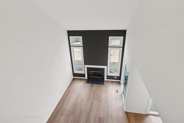 unfurnished living room featuring a fireplace with flush hearth, wood finished floors, and baseboards