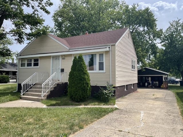 view of front of house featuring a shingled roof, a front yard, and a detached garage