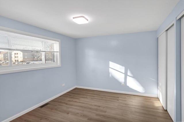 unfurnished bedroom with a closet, wood finished floors, visible vents, and baseboards